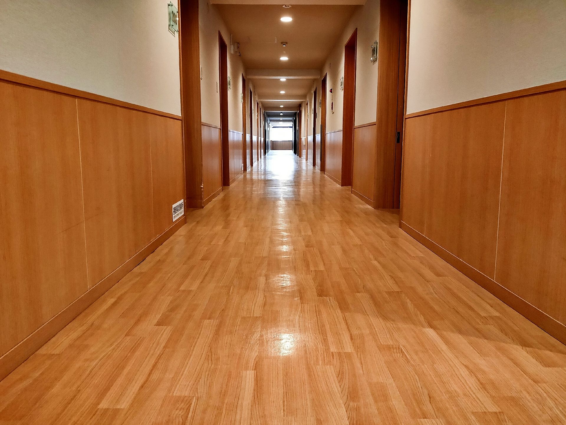 まっすぐな廊下の両サイドに居室が並んでいて、防災設備も設置されている。突き当りには窓もある。