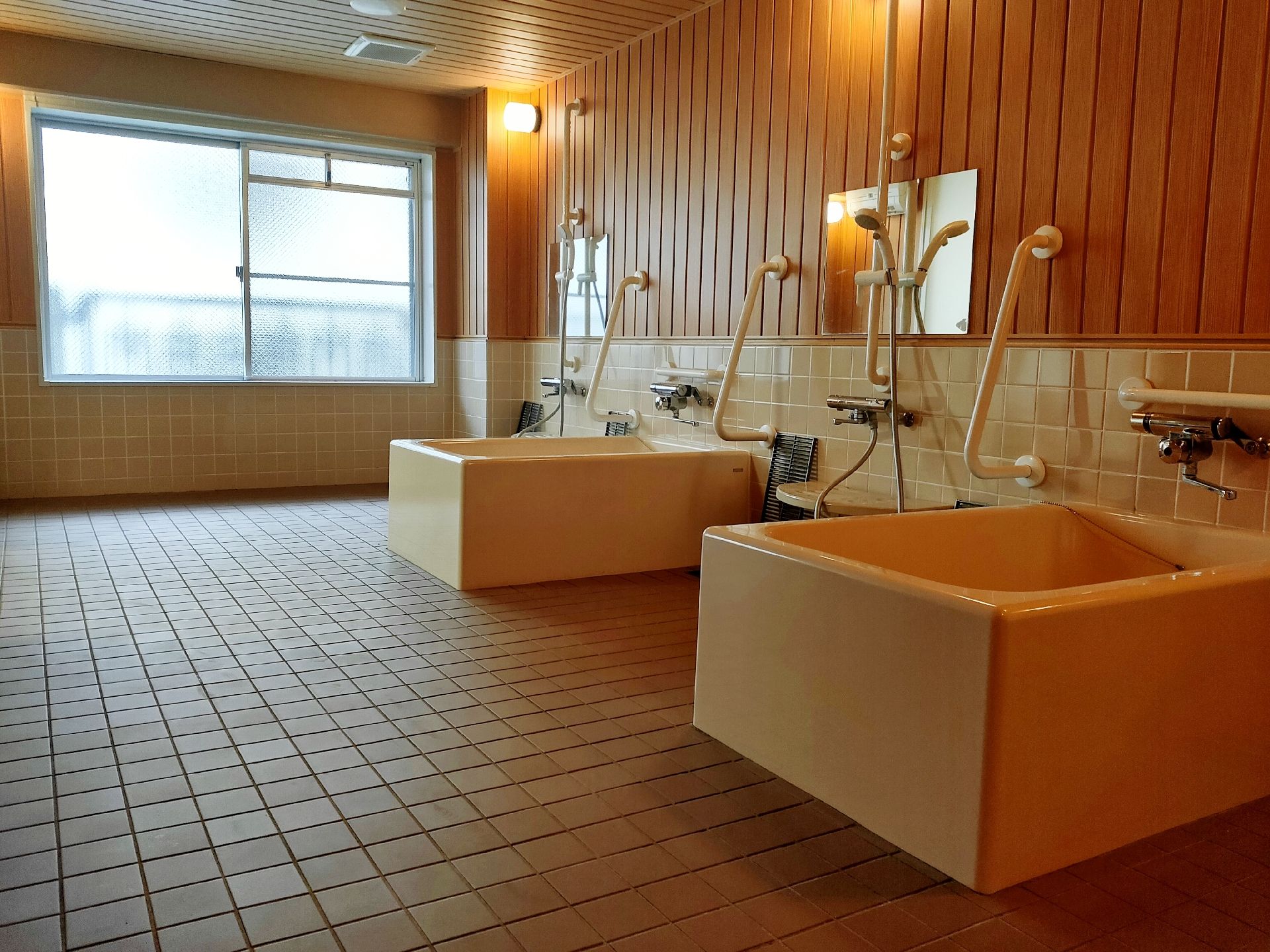 一人用の浴槽が２つ設置された広い浴室。それぞれの浴槽のそばにはシャワーや手すりもあり、大きな窓もある。