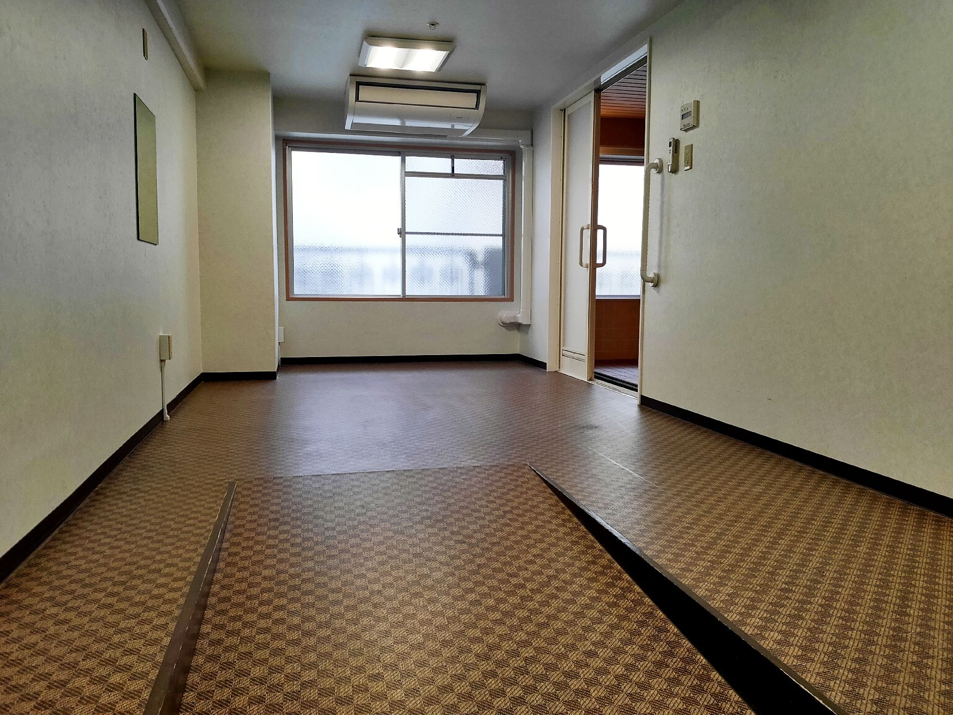 大きなエアコンが設置された広い脱衣所。右側には浴室へ続くドアがあり、そのそばには手すりがある。