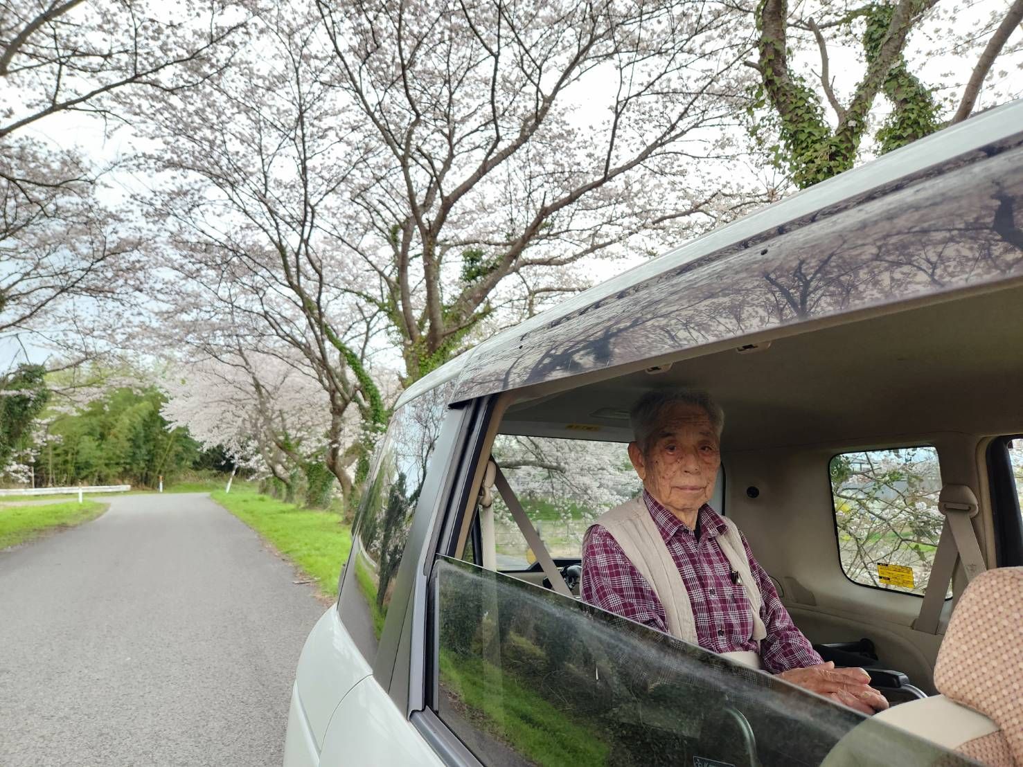 自然豊かな場所を車いすで散歩している高齢男性とそれを補助しながら話している女性スタッフ