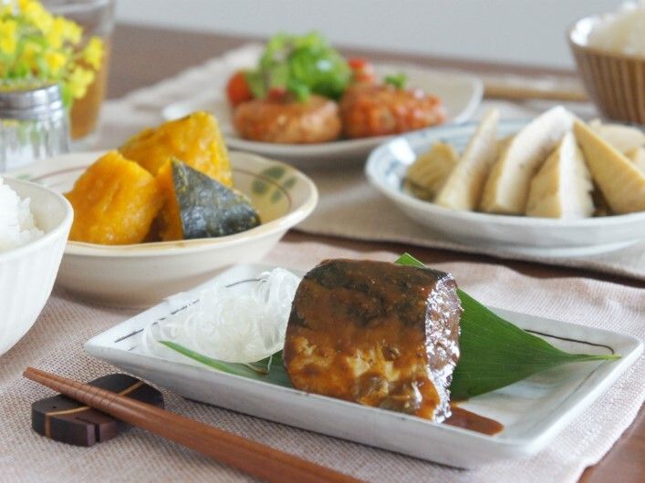 箸が箸置きの上に置かれ、サバの味噌煮やタケノコの煮物、かぼちゃの煮つけ、白ご飯などが並べられている。