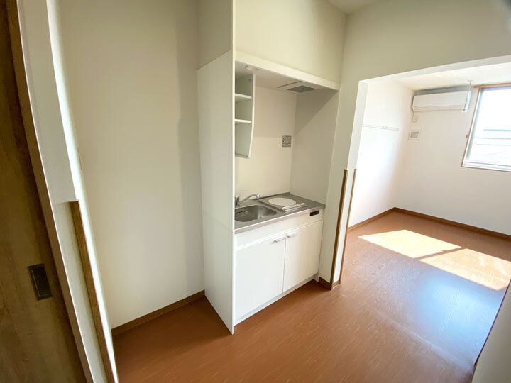 フローリングの部屋には大きな窓があり、手前にはIHクッキングヒーター付きのキッチンもある。日当たりのいい部屋。