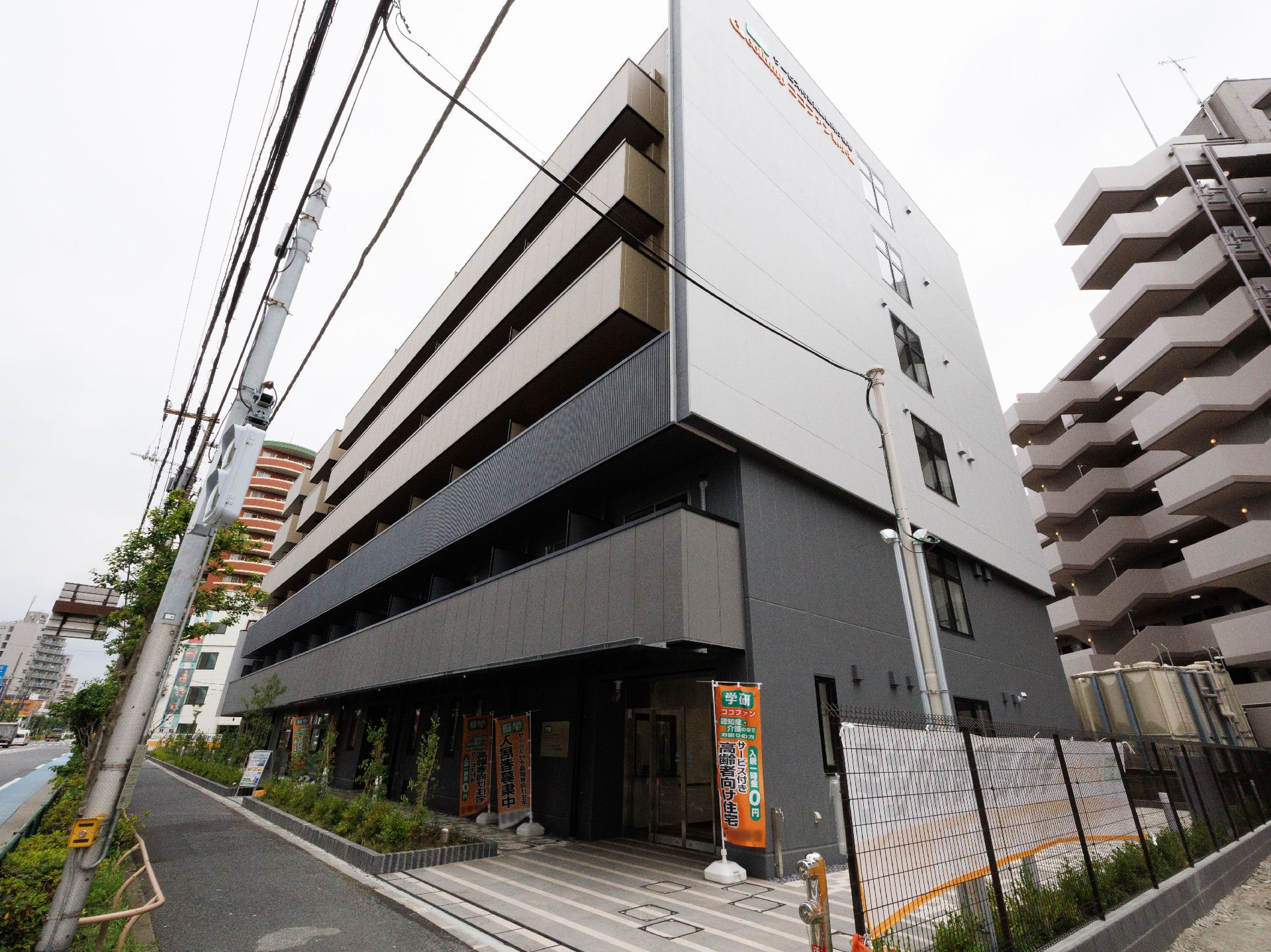 ブラウン系の重厚感のある建物の周りには草木が植えられている。周囲には背の高い建物が多くある。