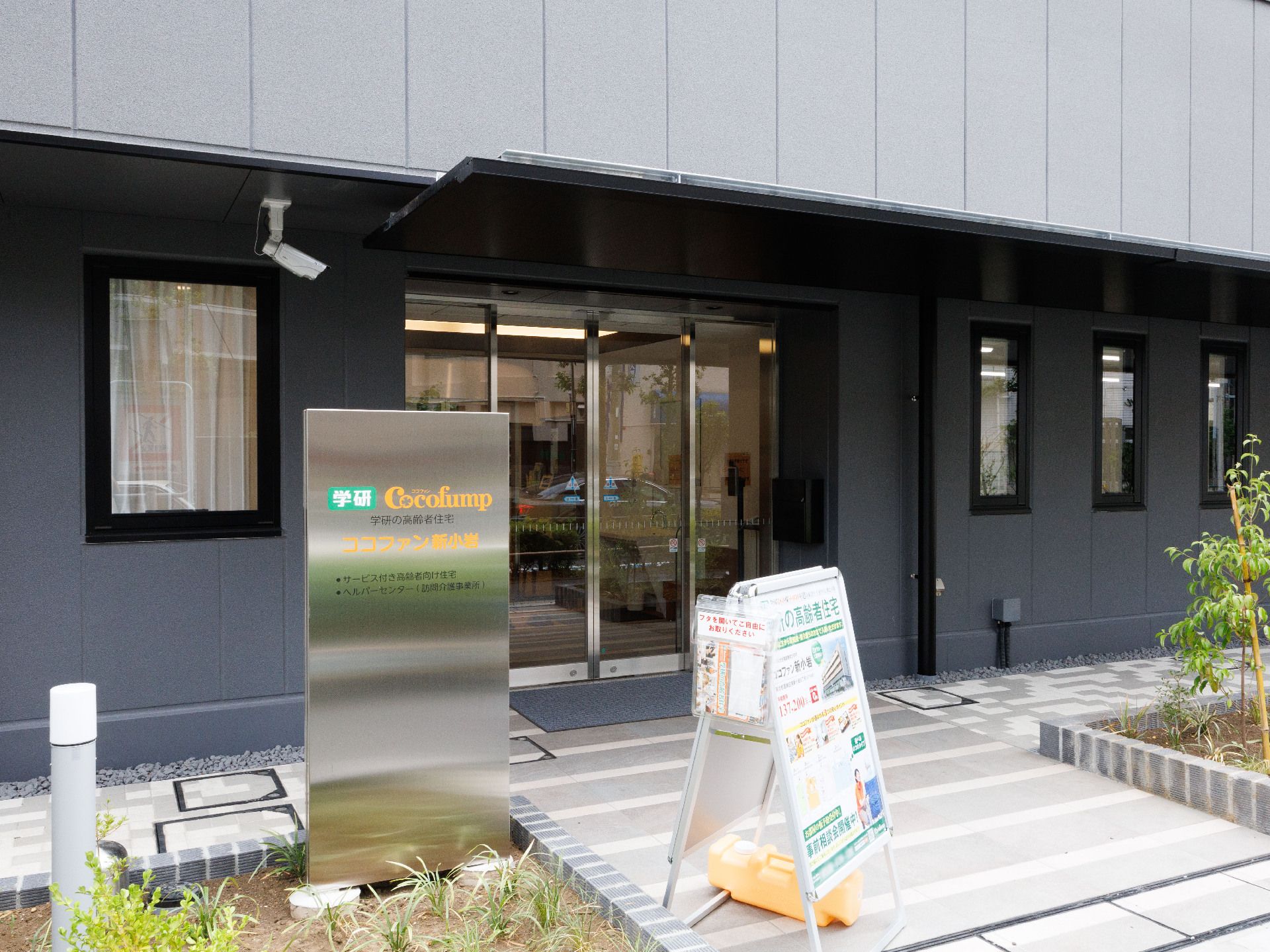 両側に花壇が置かれた道の先にある黒い建物の入り口