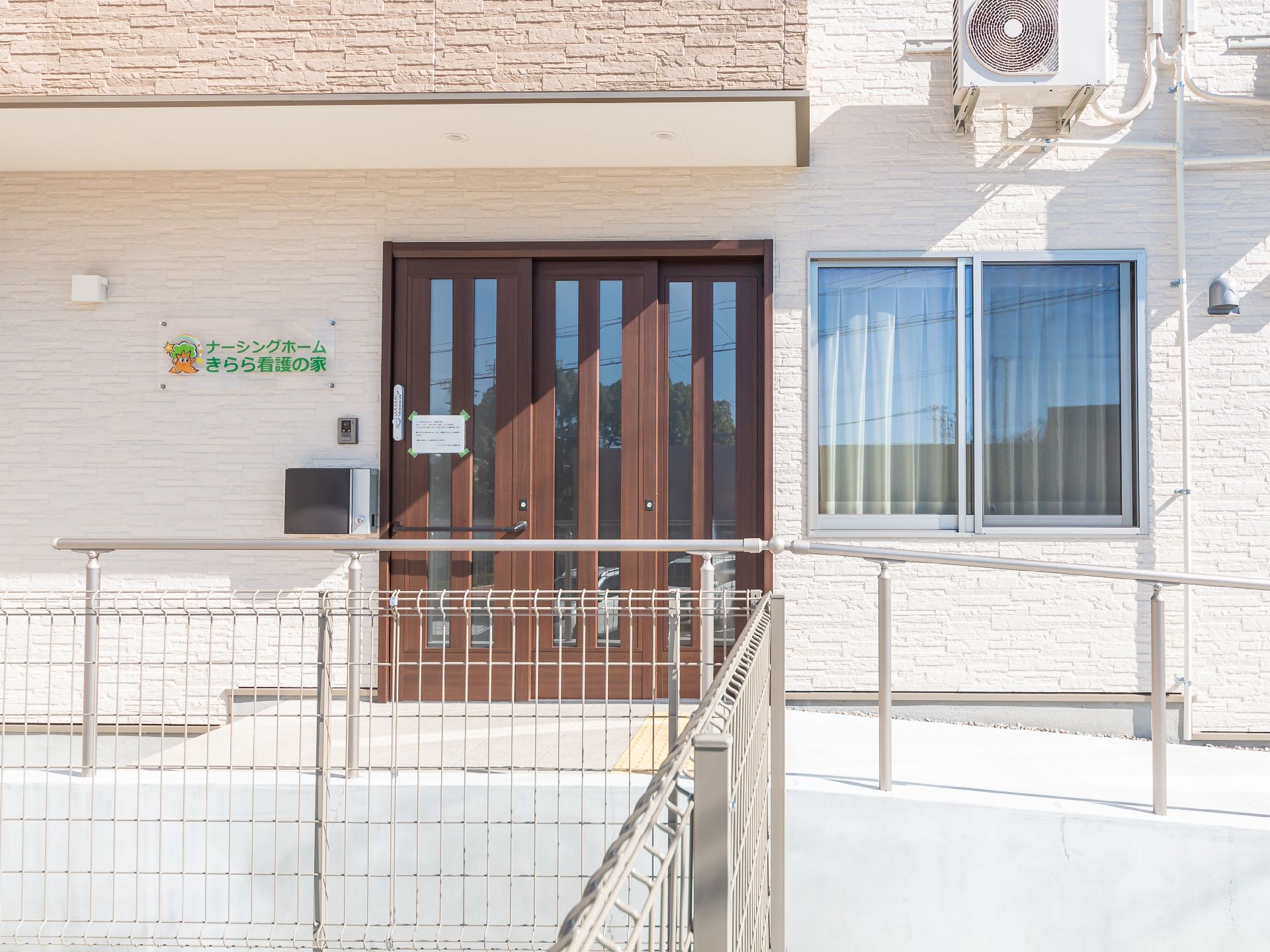 笑顔でこちらを向いている施設のスタッフと車いすに乗っている高齢者の様子。施設で写された写真