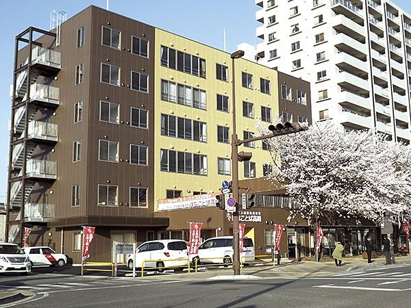 はなことば高崎と書かれている黄色と茶色ツートンカラーの外壁の6階建て建築物
