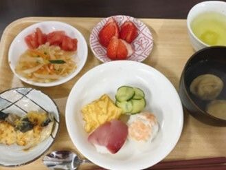 ハムエッグや野菜炒め、イチゴ、汁物、魚のピカタなどが並んだ木製のトレー。