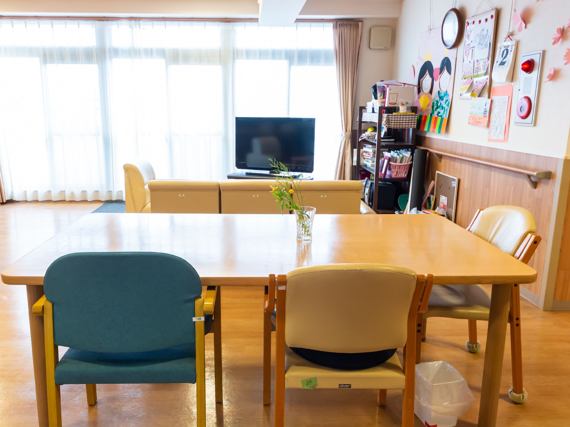 原っぱのような場所を歩いている高齢女性に付き添い笑顔で話かけているブルーのエプロンを付けた若い女性スタッフ。