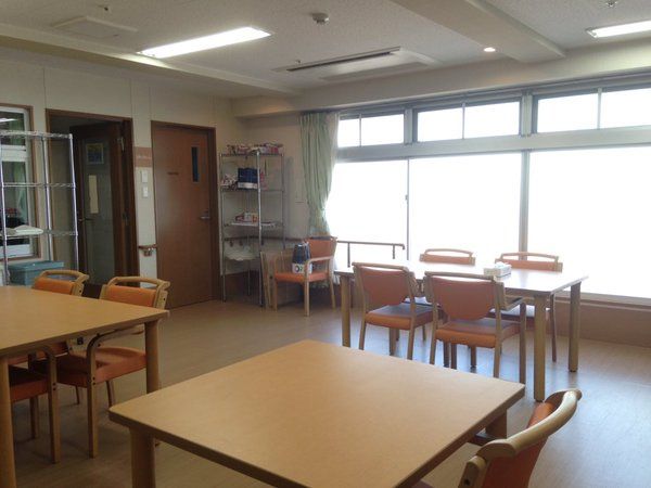大きな窓が付いた明るい雰囲気の食堂。4人掛けのダイニングテーブルセットが複数置かれている。