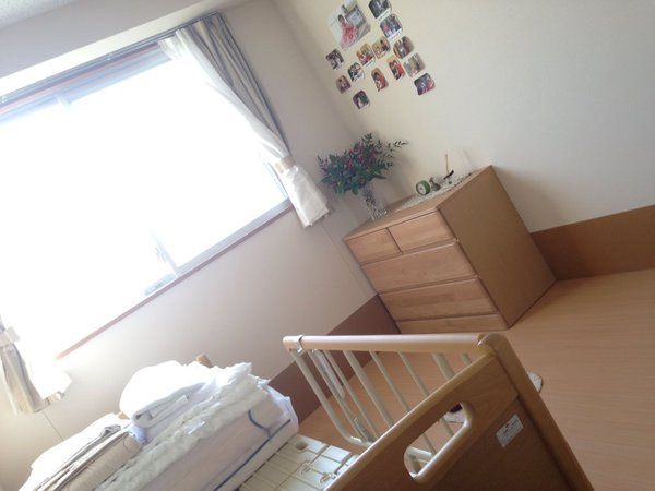寝具付きのベッドやタンスが置かれたフローリングの居室。壁にはたくさんの写真が貼られている。