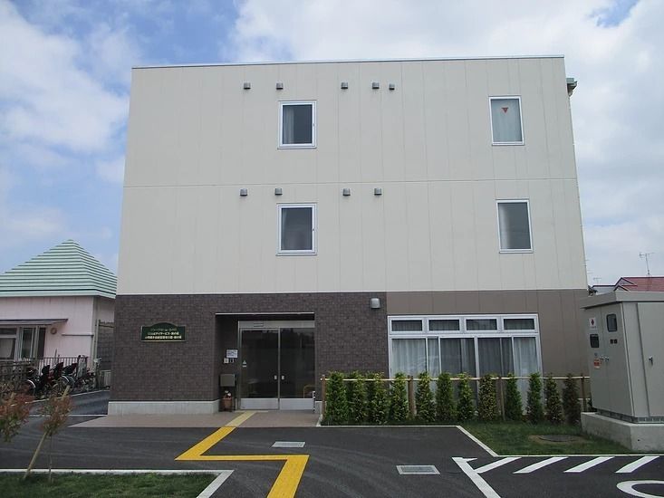 白とブラウンの３階建ての建物がある敷地内には駐車場があり、車いすマークが描かれ、点字ブロックも敷かれている。