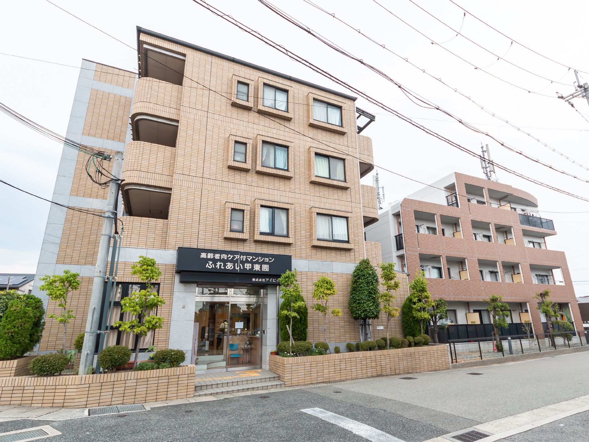 アスファルトの道路沿いに立地しているベージュ系で4階建ての建物