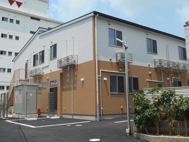 2階建ての建物は日当たりのいい場所に建っていて、各フロアにより外壁の色が異なる。敷地内には駐車スペースもある。