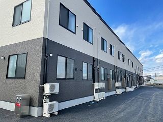 1階部分がダークグレー、2階部分が白い2階建ての建物が建つ敷地は広く、玄関には屋根が付いている。