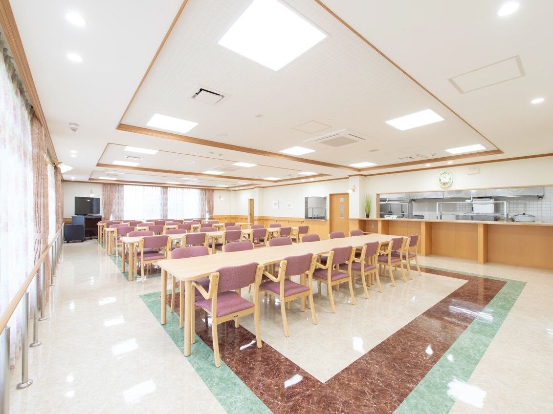 厨房がすぐそばにある食堂にはピンクの椅子がセットされたダイニングテーブルセットが複数置かれテレビもある。