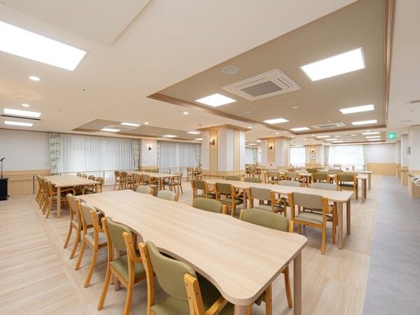 木製のダイニングテーブルセットが複数置かれた明るい雰囲気の食堂。たくさんの窓が付いている。