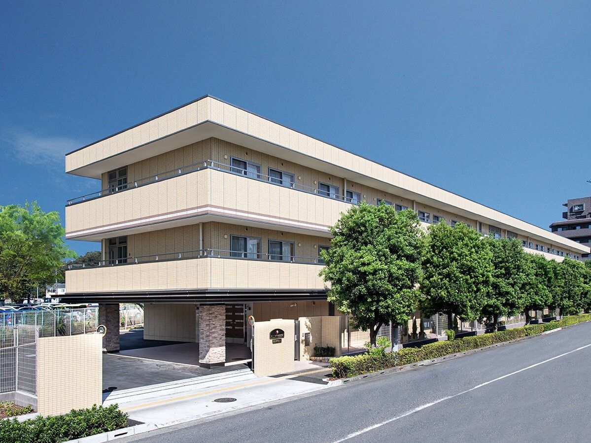 各フロアにベランダがある３階建ての建物は日当たりのいい場所に建っていて、周りには草木が植えられている。