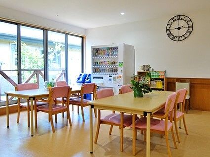 自動販売機が置かれた食堂。ピンクの椅子がセットされたダイニングテーブルセットが複数置かれている。