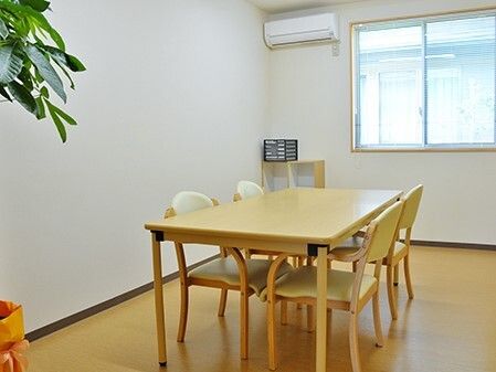 木製のテーブルセットにはいすが対面式で4脚セットされ、エアコンが付き、観葉植物が置かれている。