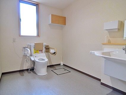 大きな窓が付いたトイレは広く、手すりや背もたれが付いた便座がある。車いす対応の洗面所もある。