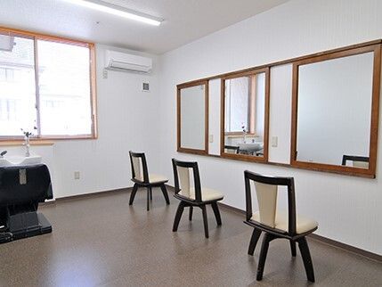 大きな鏡が3つ付いた壁の前にはいすがそれぞれ置かれ、大きな窓も付いている。洗髪台もある。