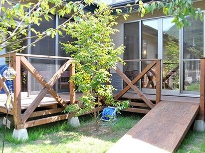 ウッドデッキのテラスから木製のスロープが庭へと続いていて、テラスの周りには木も植えられている。