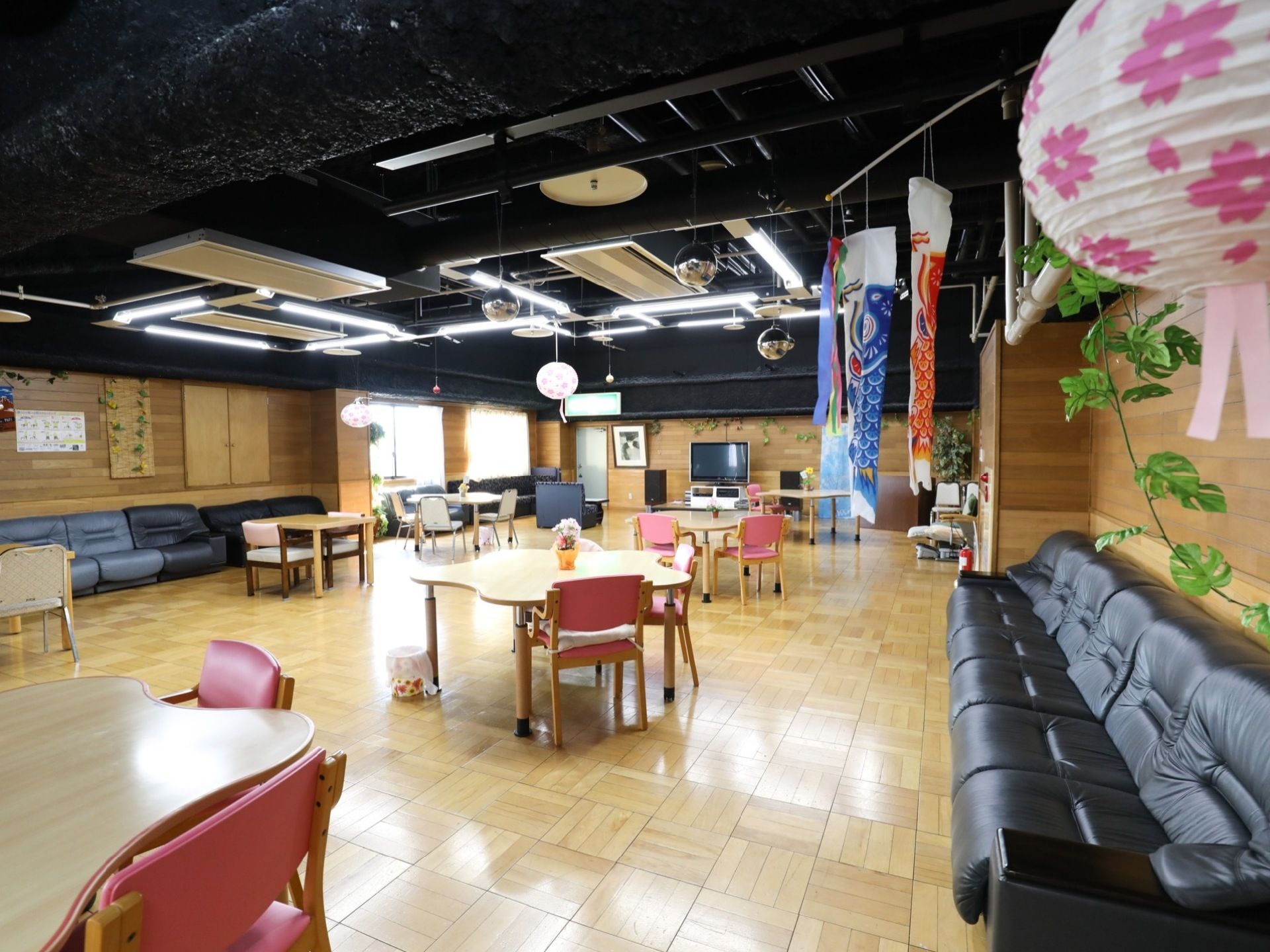 広い室内に、花形の木製テーブルが数個置かれ、椅子が並んでいる。大きな鯉のぼりが飾られている。壁沿いにソファーが並んでいる。