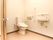 トイレ個室内の様子。温水洗浄便座付き便器があり、便座付近に操作ボタンがある。壁に手洗い場が設置されている。