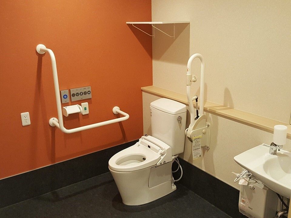 手すりや呼び出しボタンが付いた広いトイレにはふたのない便座があり、手洗い場もある。