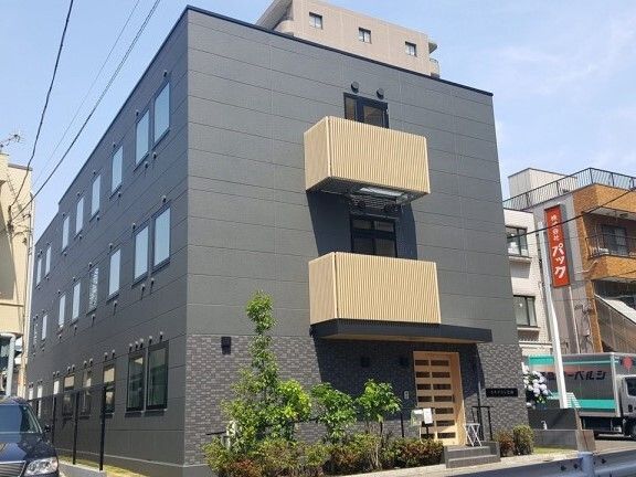グレー系の外壁で3階建ての建物の玄関には階段が設置され、周りには草木が植えられている。