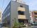 グレー系の外壁で3階建ての建物にはたくさんの窓があり、玄関には屋根があり、階段も付いている。