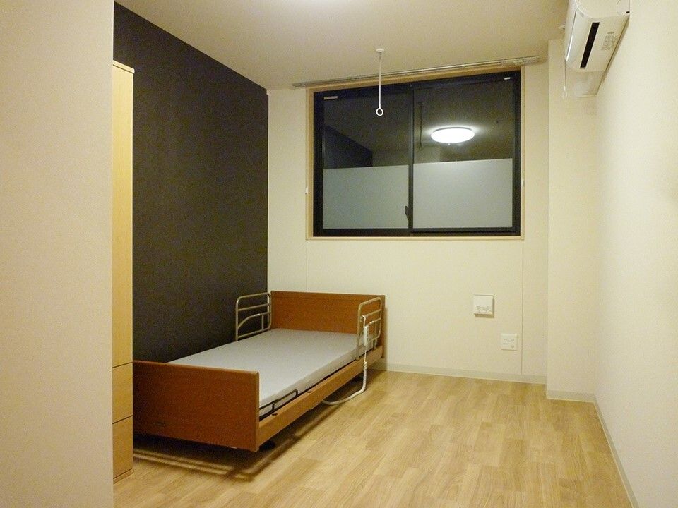 おおきな窓が付いているフローリングの部屋。介護ベッドやクローゼットが置かれている。
