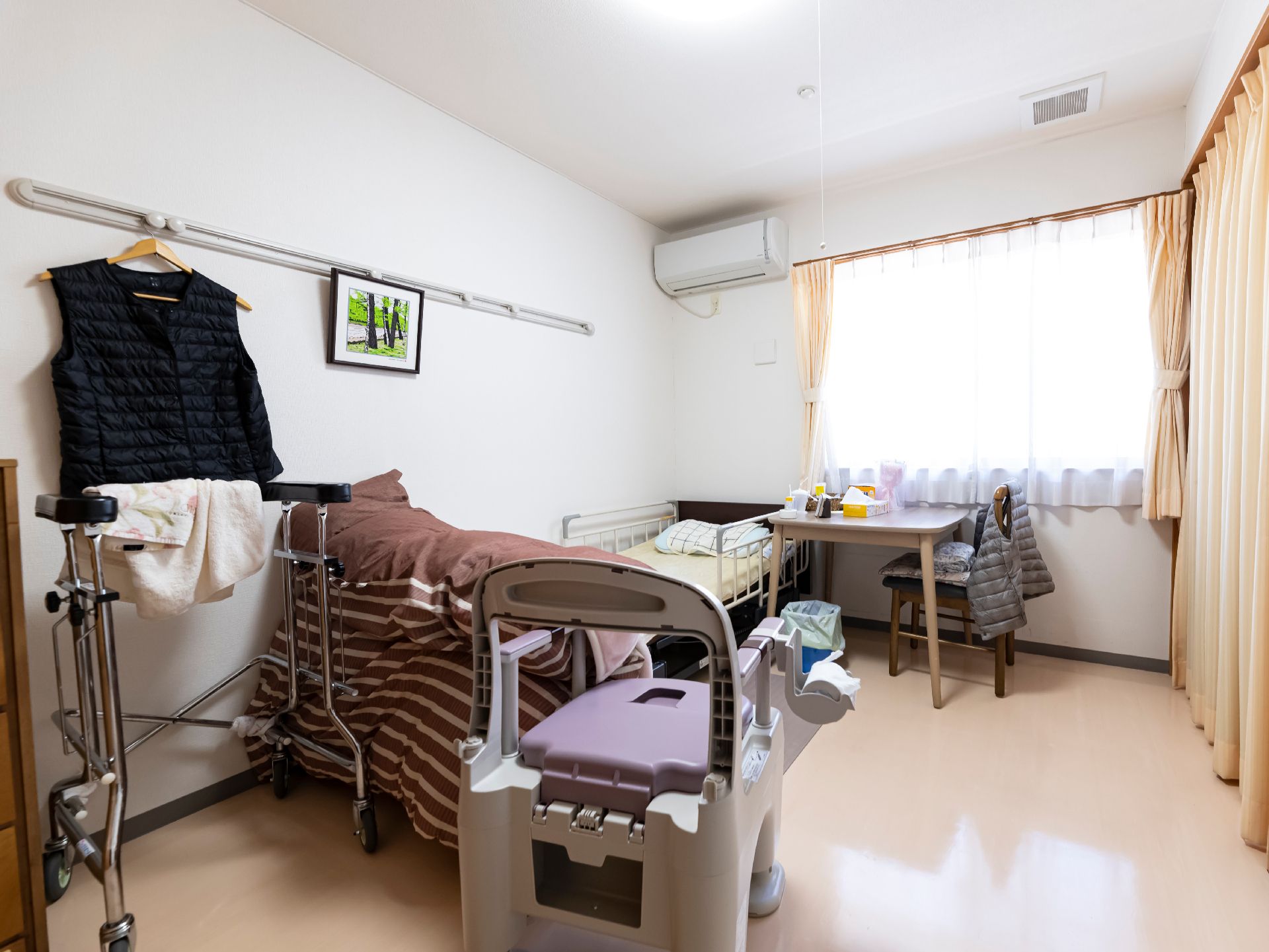 緑の多い屋外の遊歩道で散歩を楽しんでいる車いすの高齢女性と付き添いのピンクのエプロンを付けた女性スタッフ。