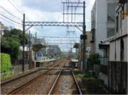 複線の線路の両側には検見川駅のホームがあり、手前には踏切がある。周辺には民家があり、緑も豊富である。