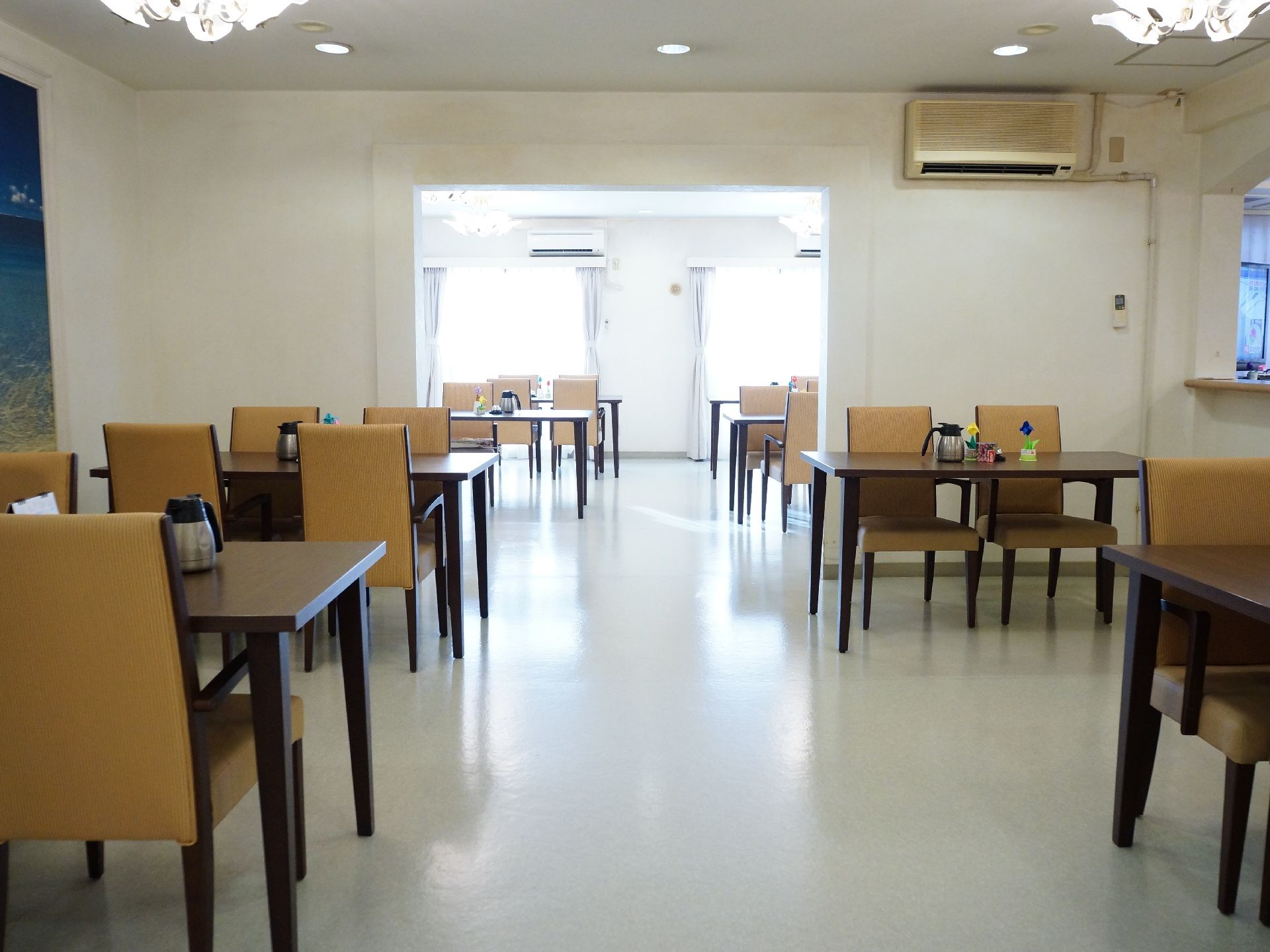 食堂のテーブルの上には、それぞれポット・調味料などが置いてある。茶色のテーブルには、黄土色のシートの椅子がセットされている。