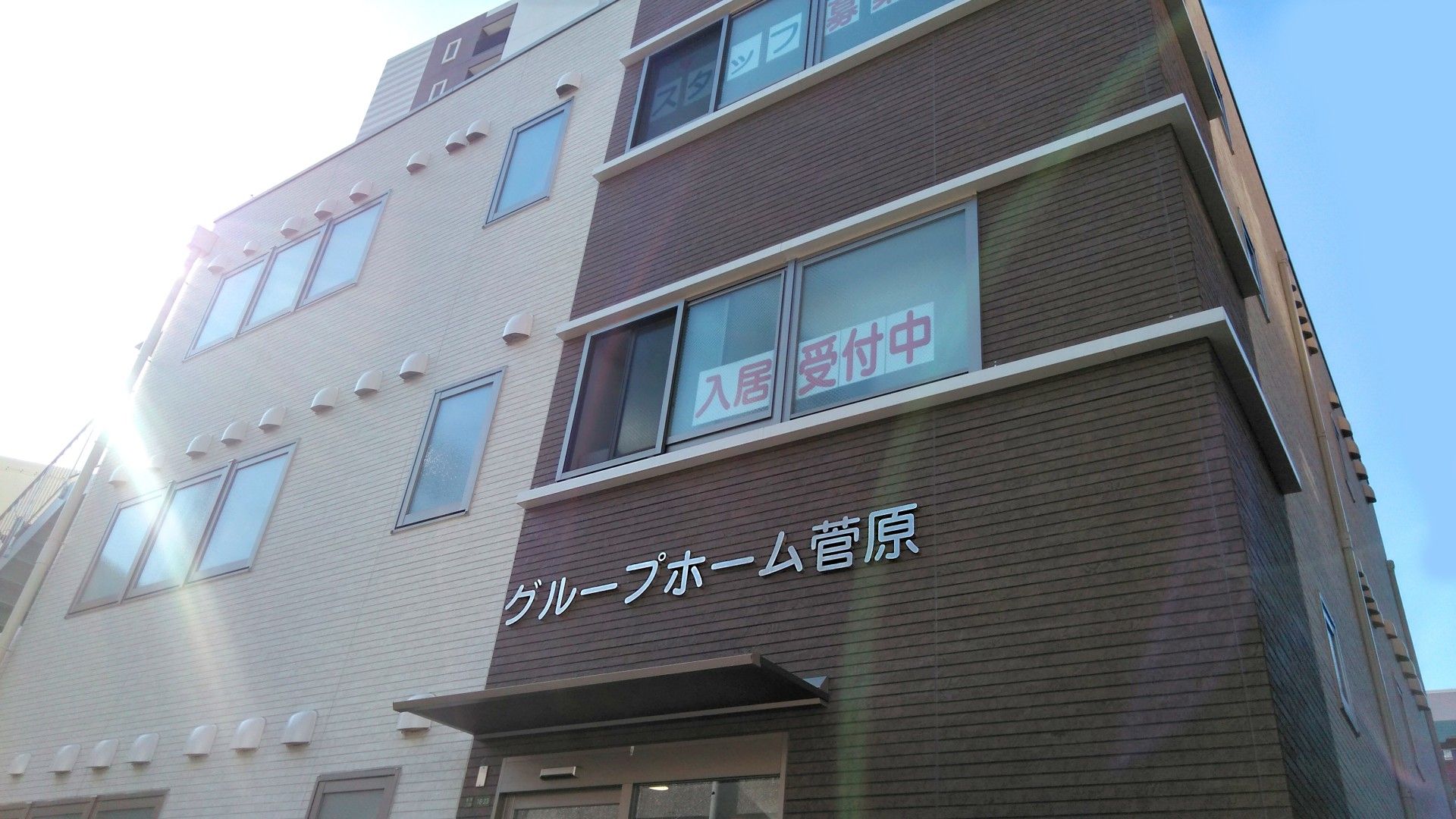 高齢女性たちと白衣を着た女性スタッフがソファの周りに集まり、楽しそうに話している。
