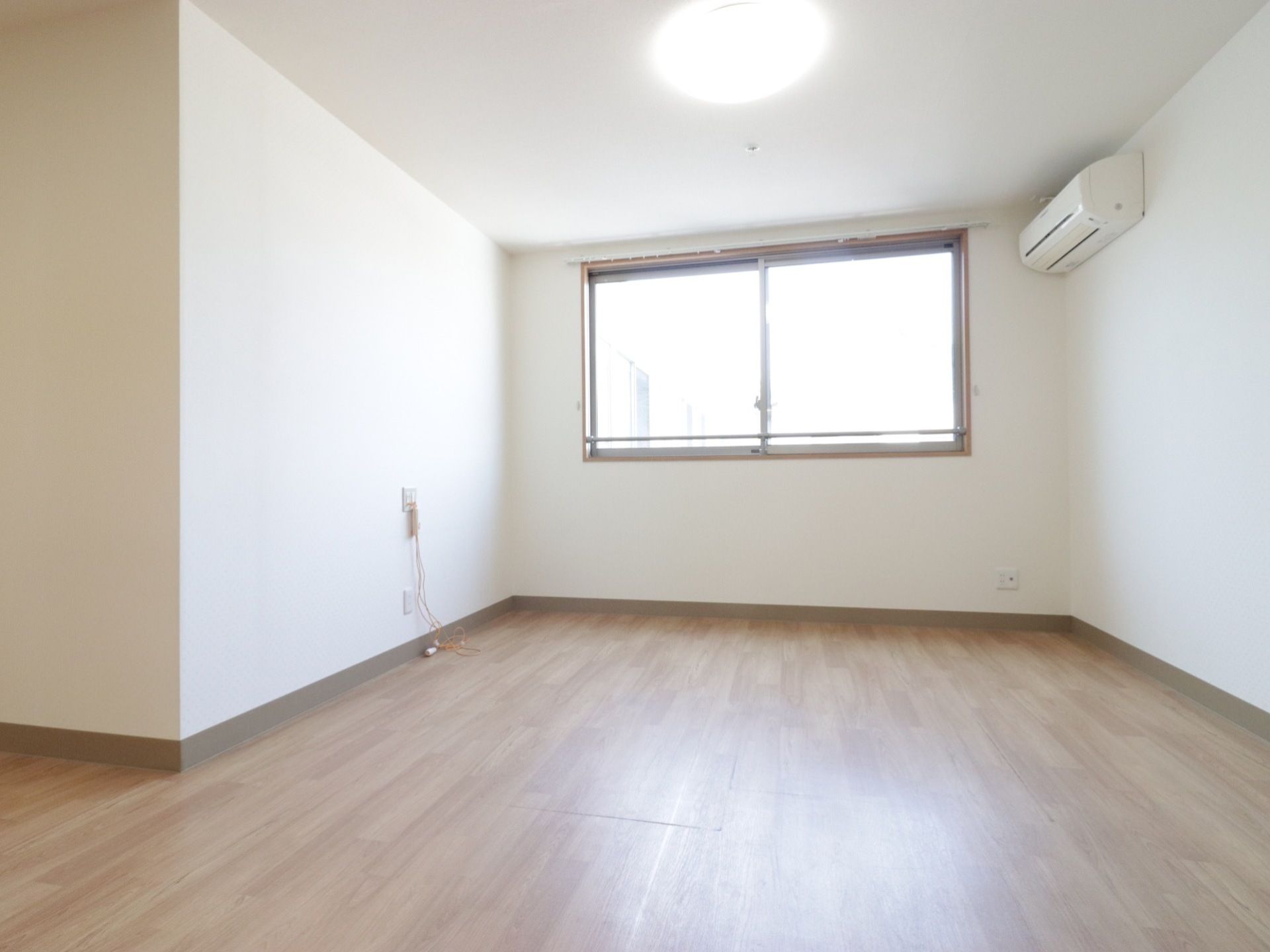突き当りに横長の腰高窓がある部屋である。シーリングライトが天井にある。壁は白く、上部にエアコンがある。