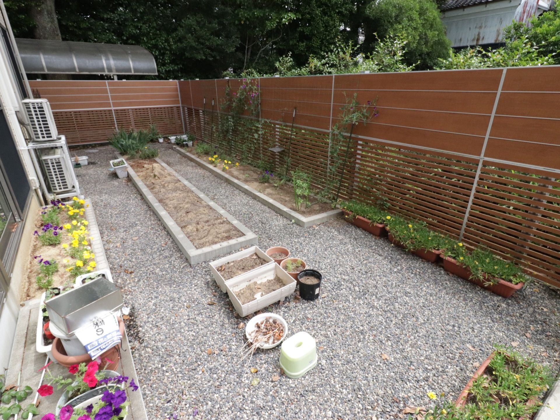 グレーのコンクリートで囲われた長方形の花壇がある。茶色いプランターでは花が咲いている植物を育てている。