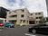 3階建ての灰色の外壁の建物である。施設前には専用の駐車場が確保されている。プランターには植物が植えられている。