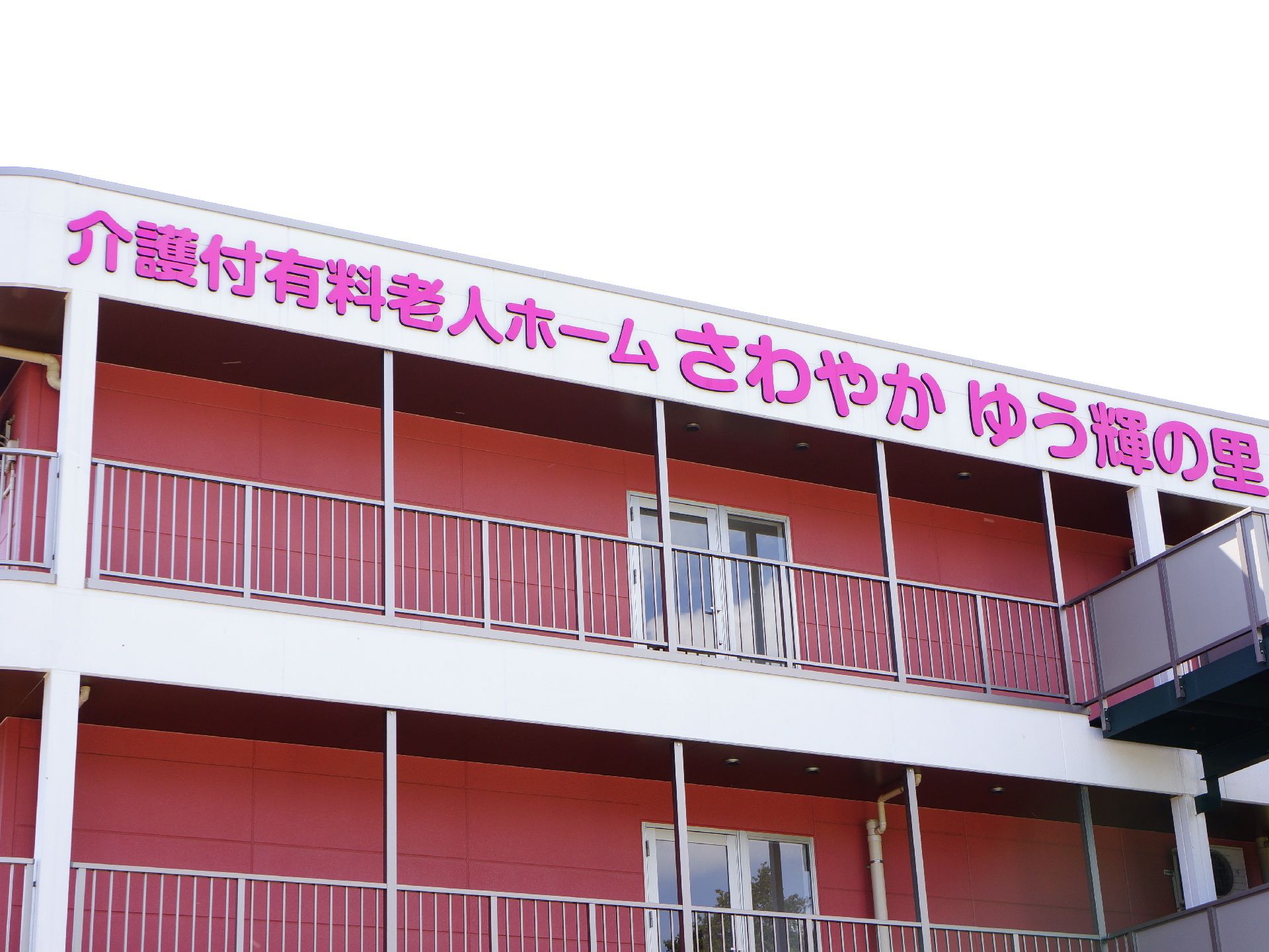 建物の壁面最上部に設置された、施設名の描かれた鮮やかなピンク色の文字看板