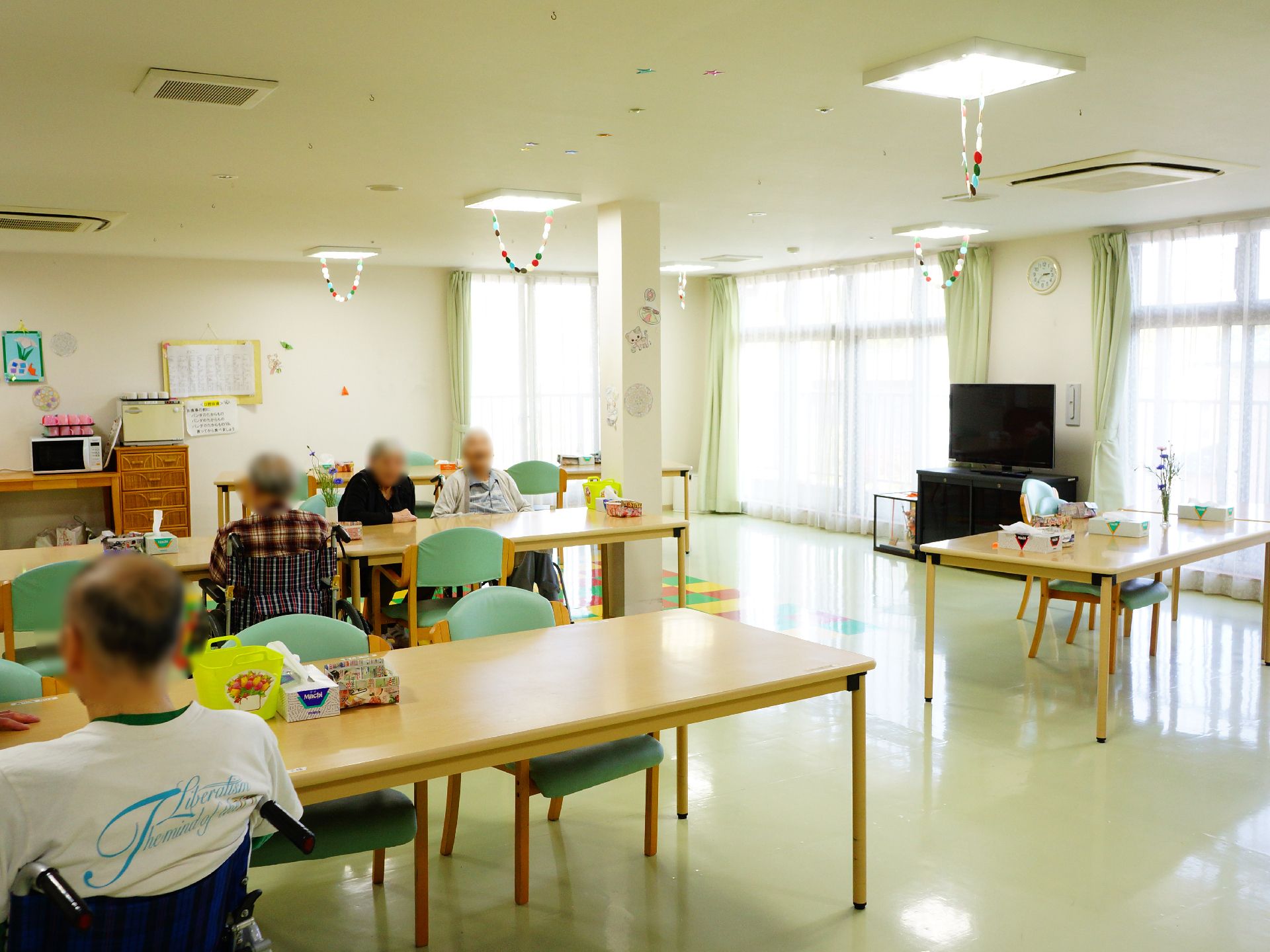 窓から明るい光の差し込む交流スペースでくつろいだ様子の入居者