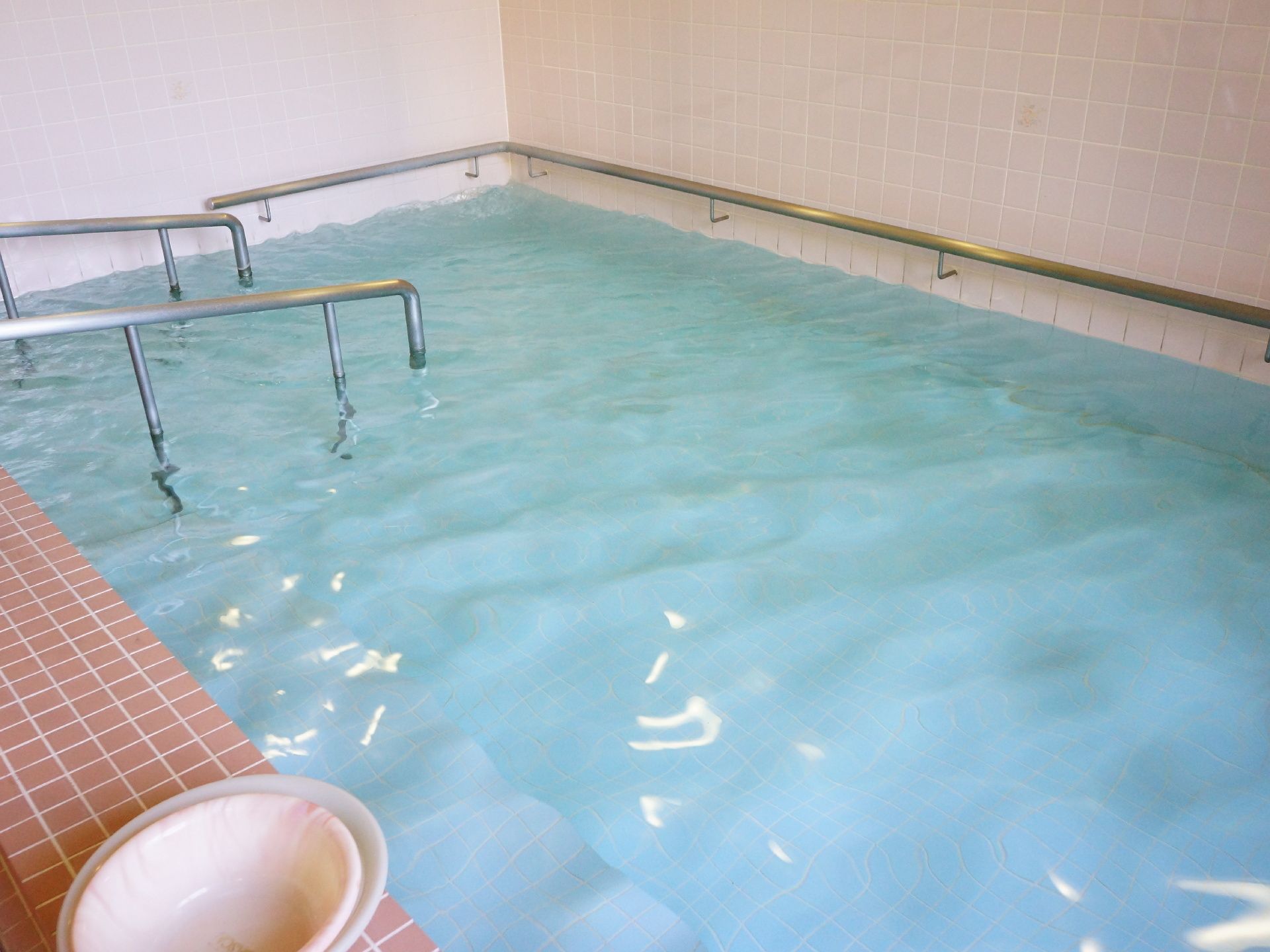 浴槽の床は白色である。お湯がきれいなので床の色もよく解る。また手すりが浴槽の周りにしっかりと設置してある。