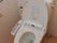 白のタイル壁にフローリングで清潔感がある。トイレには温水シャワー機能がついている。壁には立ち座りしやすい位置に手すりを配置している。