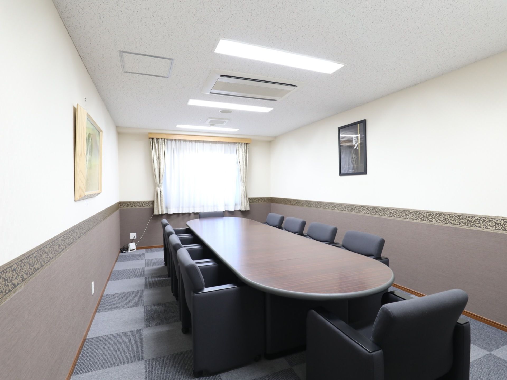 落ち着きのある室内には、大きな長テーブルと椅子が並べられている。窓にはカーテンが掛けられ、壁には絵画が飾られている。