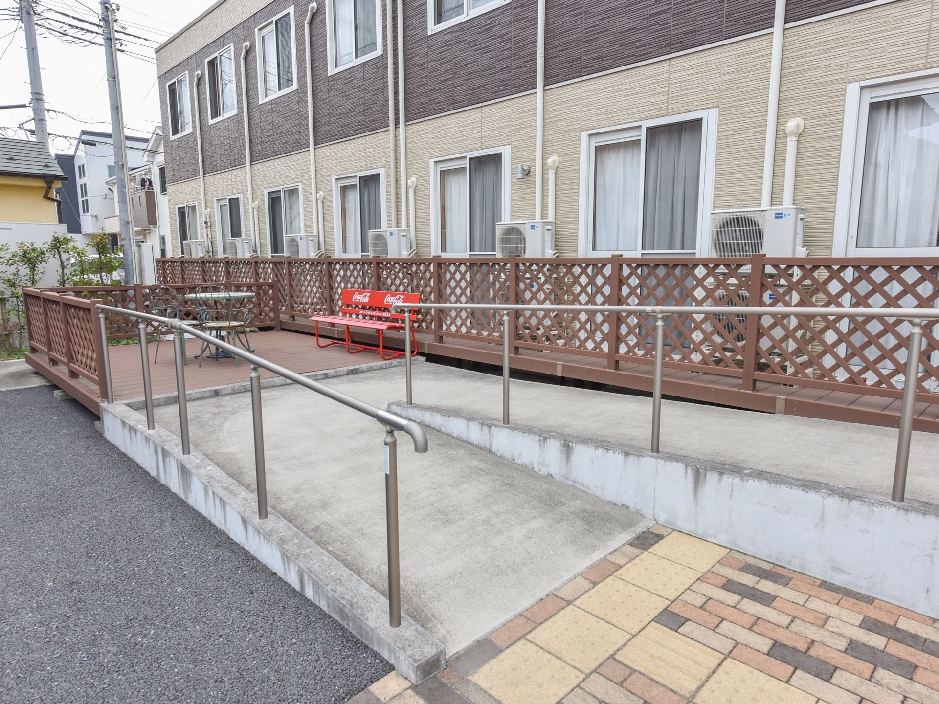 ゆるやかなスロープには手すりが取付けられている。スロープの先には丸いテーブルや椅子、ベンチが並べられている。