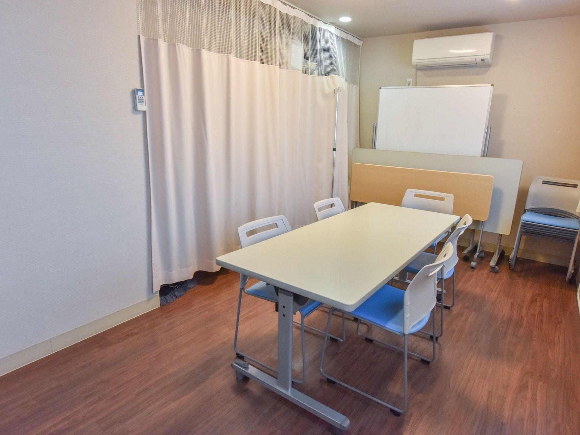 談話室の中央にテーブルと椅子が並べられている。ホワイトボードの近くには折りたたまれたテーブルが2台置かれている。重ねられた椅子もある。