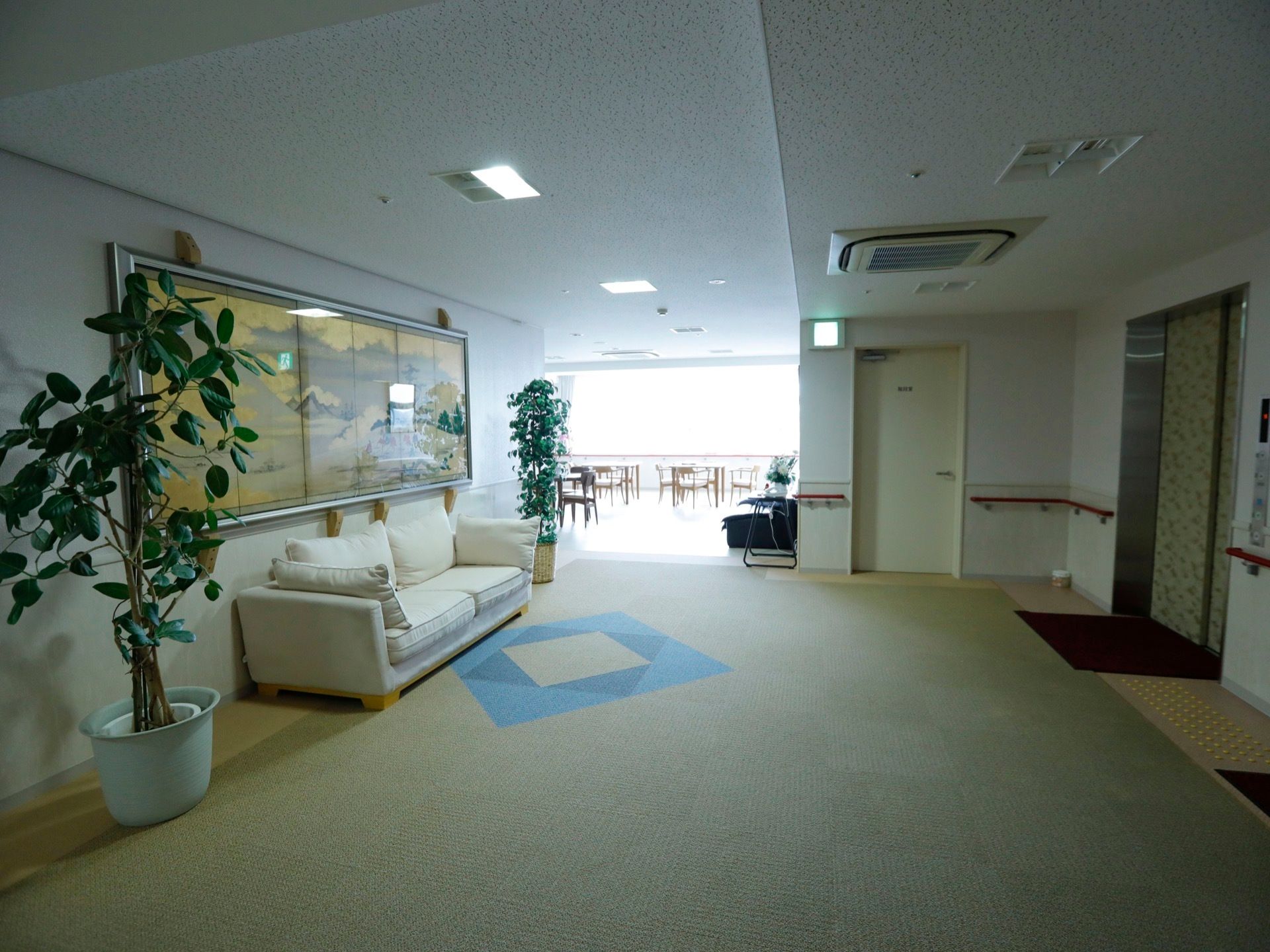 二人掛けソファーが、左側の壁の前に設置されている。エレベーターの扉は、お洒落なデザインになっている。両側の壁には手すりがある。