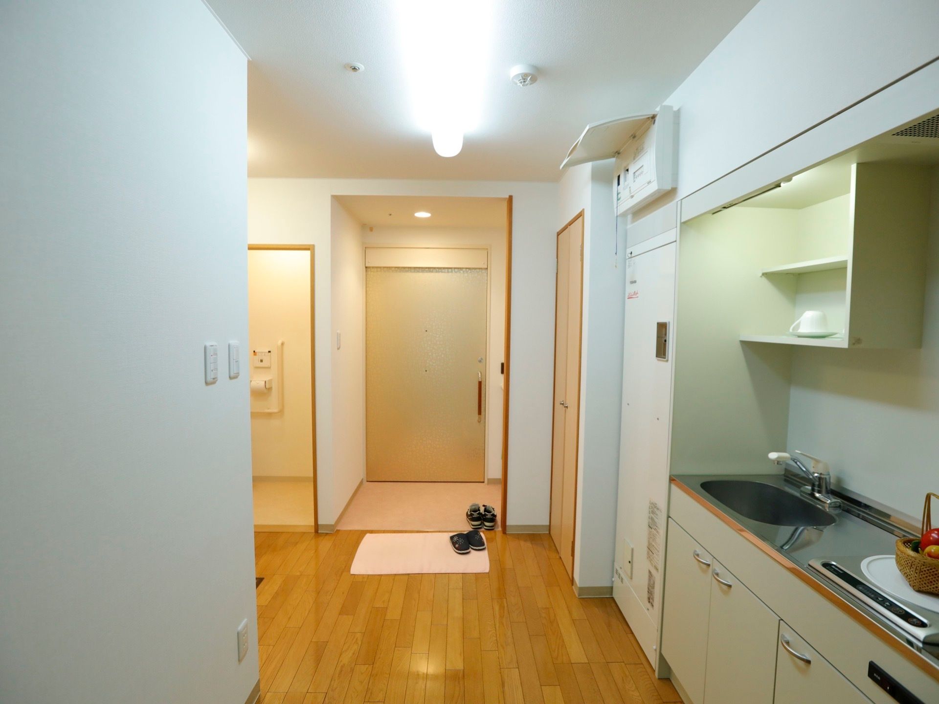 木目調デザインの居室の床は、安全なバリアフリーとなっている。玄関前には白いマットが置いてあり、右端にスリッパがある。
