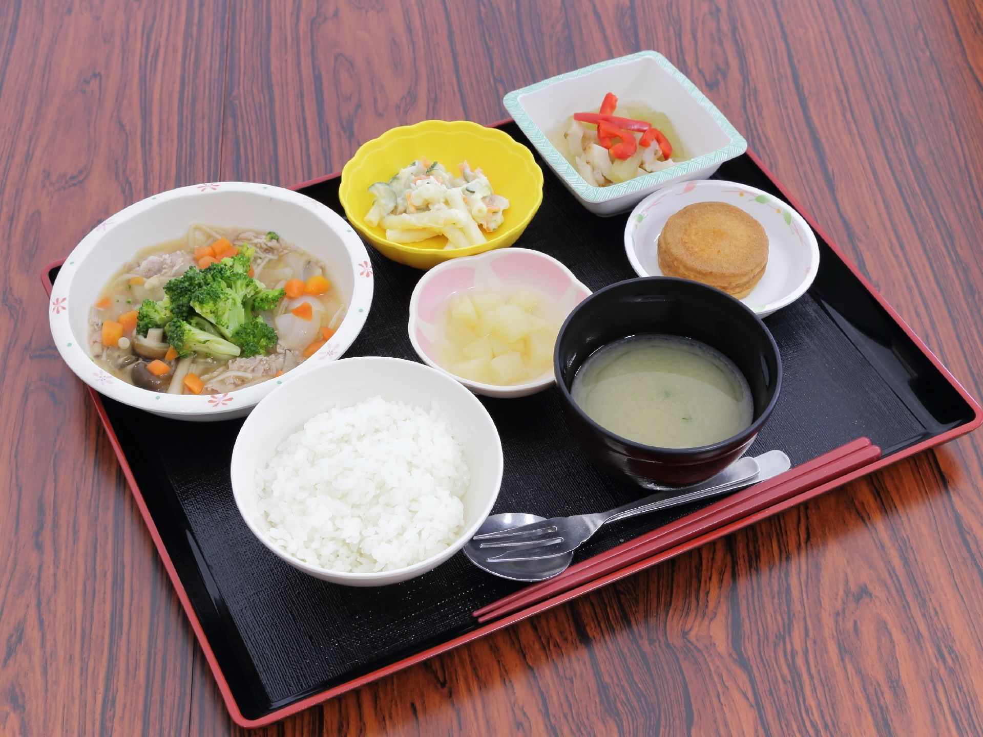 食事メニューは、ごはんとみそ汁の他に野菜スープやマカロニサラダがあり、箸の他にスプーンとフォークが並べられている。