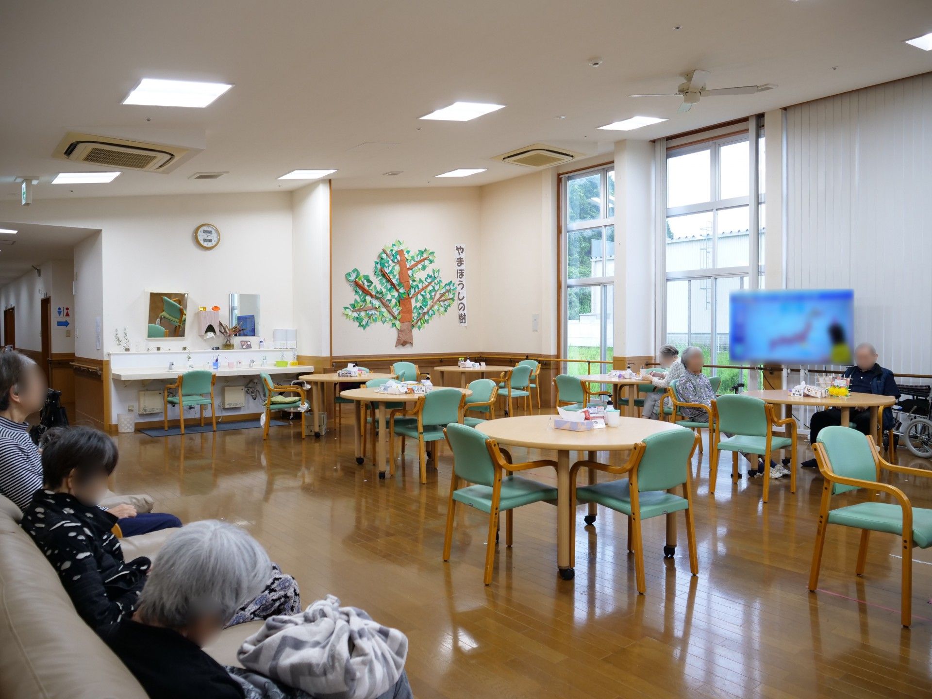 高齢者の方にタオルをかけてマッサージしているスタッフと振り返りながら会話する女性の様子